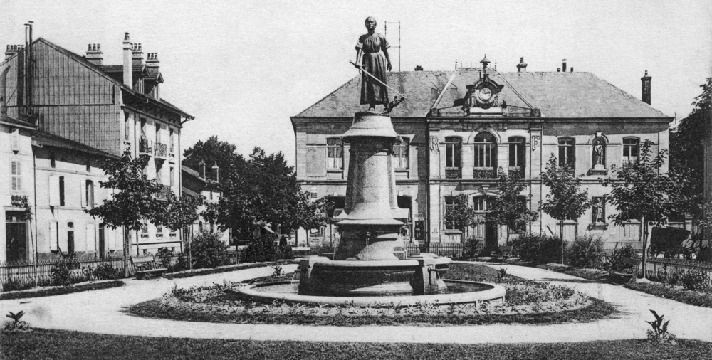 Épinal. La bourse de commerce derrière la statue de Jeanne d’Arc. Aujourd’hui, n’existe plus que le centre de la façade, sur un bâtiment abritant l’espace judiciaire Julie Victoire Daubie. Carte postale des années 1910, collection Mémoire Vive.