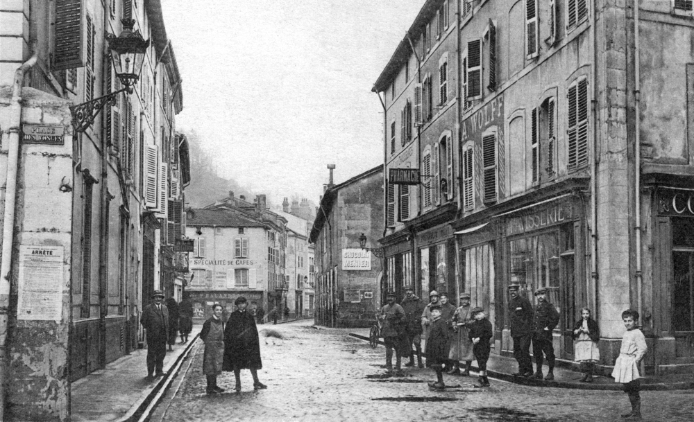 Épinal. La rue des Halles vue depuis la place des Vosges. À droite, derrière le garçon en noir et le militaire en imperméable, entre la pâtisserie et la pharmacie, le magasin d’A. Wolff. Carte postale voyagée en juin 1918. Collection Mémoire Vive.
