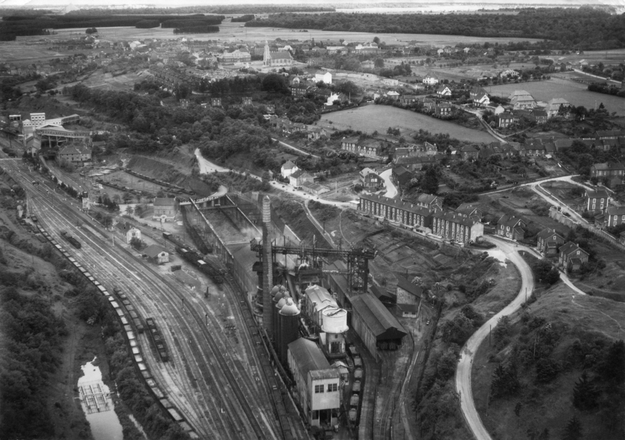 Hussigny. Au premier plan, les hauts-fourneaux et la gare. À l’arrière plan une cité ouvrière et le village. Carte postale d’après-guerre, collection mémoire Vive.