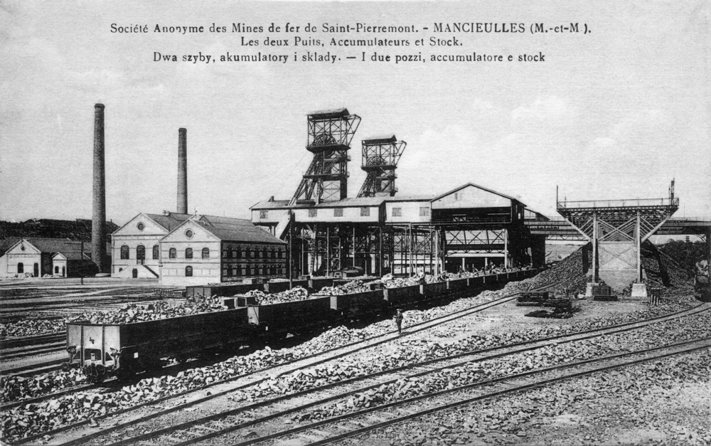 Mancieulles. Les deux puits, accumulateurs et stock de la Société anonyme des mines de fer de Saint-Pierremont. Prenant en compte l’importance des travailleurs immigrés, la légende est également rédigée en polonais et en italien. Carte postale des années 1900. Collection Mémoire Vive.