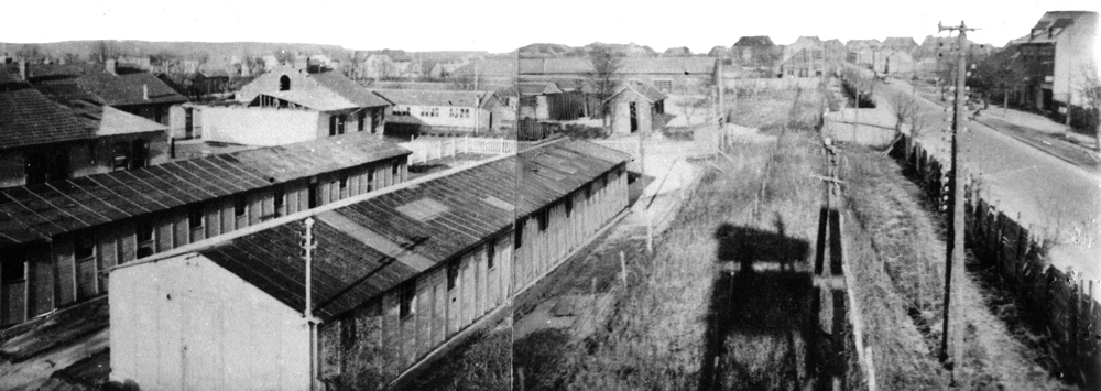 Un angle du camp de Royallieu vu depuis le mirador central dont l’ombre se profile sur le sol. Le renfoncement à droite dans la palissade correspond à l’entrée du Frontstalag 122.