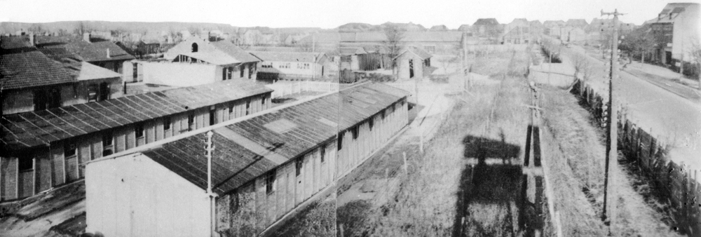 Un angle du camp de Royallieu vu depuis le mirador central dont l’ombre se profile sur le sol. Le renfoncement à droite dans la palissade correspond à l’entrée du Frontstalag 122.
