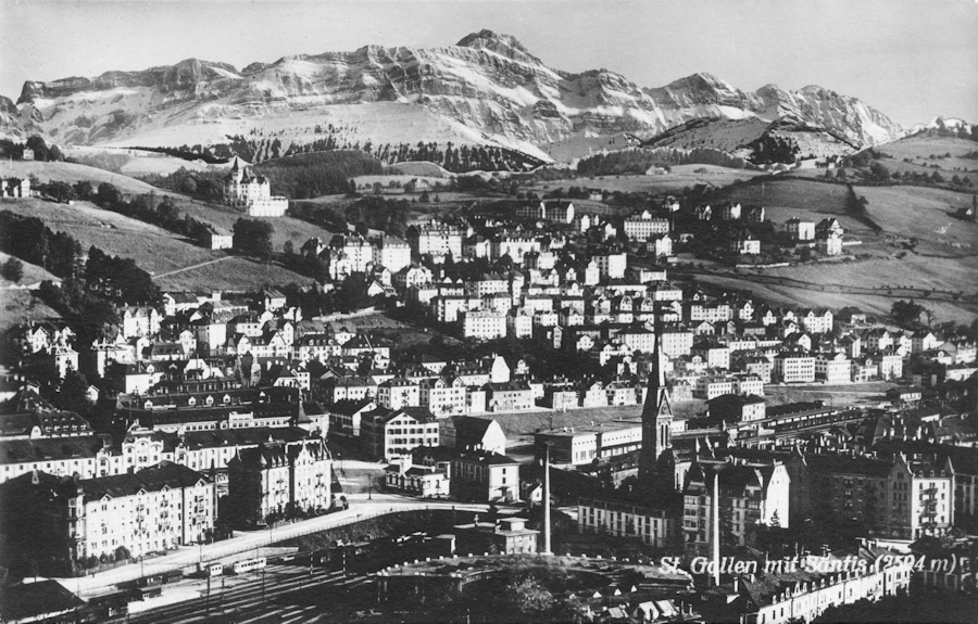 Saint-Gall, avec, incrusté au fond par photomontage, la barrière calcaire du Säntis (2502 m). On distingue la voie ferrée qui traverse la ville. Carte postale des années 1940, collection Mémoire Vive.